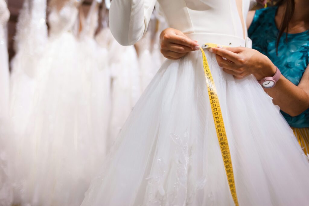 Consultant of the salon of wedding dresses takes measurements of the client's waist