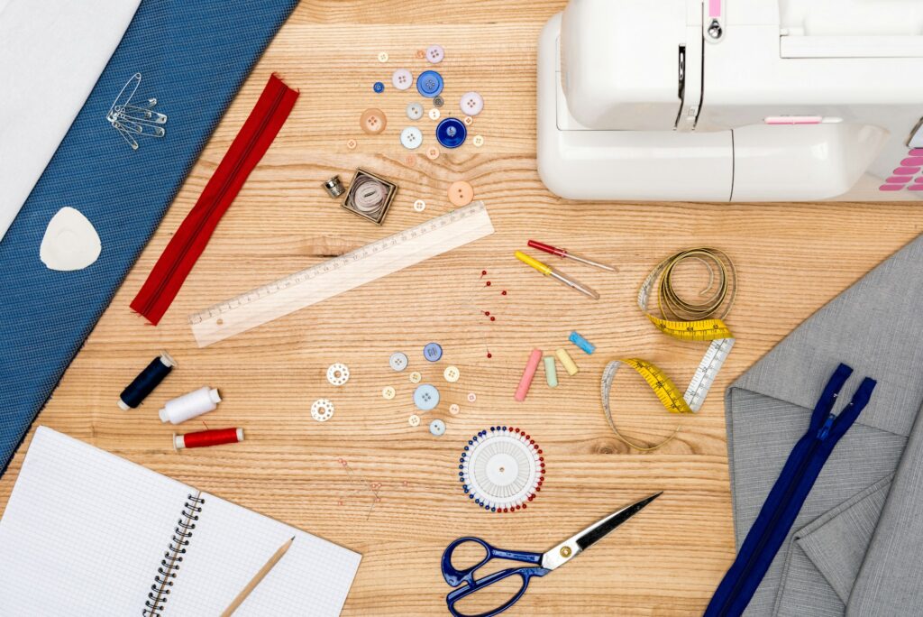 top view of sewing machine, buttons, zippers and other various tailoring items on wooden tabletop